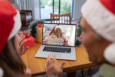 Noel Baba şapkalı beyaz bir baba ve kızı mutlu Afro-Amerikan bir kadınla görüntülü görüşme yapıyorlar. Noel, kutlama ve dijital kompozit görüntü.