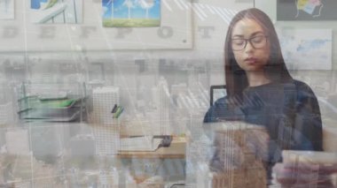 Bir kadın yönetici ofiste cep telefonu kullanırken görülüyor. Finansal grafikler ve veriler arka planda, küresel ekonomi ve ticareti temsil eden veriler gösterilmektedir..
