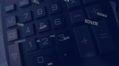 Siyah bir arkaplan karşısında birden fazla sayının canlandırılması. Siyah bir hesap makinesi düşer ve yavaş çekimde sayılar ve grafiklerle kağıtların üzerinde zıplar.