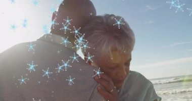 Plajdaki çift ırklı yaşlı çiftin üzerinde yılbaşı kar taneleri animasyonu. Noel, gelenek, kutlama ve şenlik kavramı dijital olarak oluşturuldu.