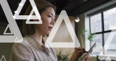 Ofiste dijital tablet kullanarak Asyalı iş kadınının üzerinden geçen beyaz üçgenlerin animasyonu. Dijital bileşik, çoklu pozlama, girişimci, sanat, iş dünyası, tasarım ve teknoloji kavramı.