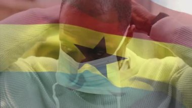 Gana bayrağının animasyonu. Yüz maskeli Afro-Amerikan bir adam üzerinde. Küresel vatanseverlik, salgın hastalık ve dijital arayüz kavramı dijital olarak oluşturulmuş video.