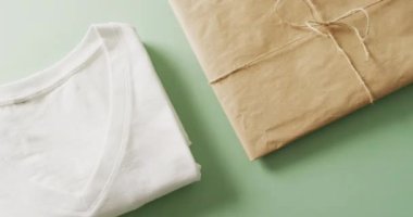 Yeşil arka planda kahverengi kağıt parselli beyaz katlanmış tişört videosu. Giyim, moda, perakende, kumaş, doku ve malzeme konsepti.