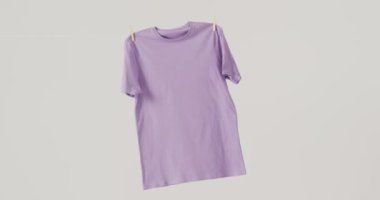 Beyaz arkaplanda asılı mor tişörtün yakın çekim videosu. Giyim, moda, perakende, kumaş, doku ve malzeme konsepti.