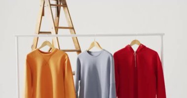 Beyaz arka planda asılı sarı, mavi ve kırmızı kazak videoları. Giyim, moda, perakende, kumaş, doku ve malzeme konsepti.