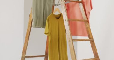Hardal, yeşil ve turuncu tişörtlerin beyaz arkaplanda asılı olduğu bir video. Giyim, moda, perakende, kumaş, doku ve malzeme konsepti.