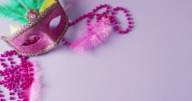 Pembe maskeli maskeli, tüylü ve eflatun arkaplanlı, eflatun arkaplanlı Mardi Gras boncuklu bir video. Karnaval, kostüm, parti malzemeleri, eğlence ve kutlama konsepti..
