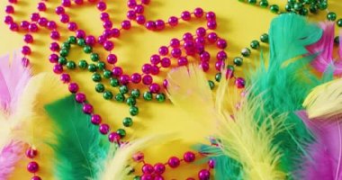 Sarı arka planda pembe ve yeşil Mardi Gras karnaval boncukları ve tüylerinin videosu. Karnaval, kostüm, parti malzemeleri, eğlence ve kutlama konsepti..