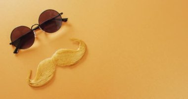 Sarışın sahte bıyıklı ve sarı arka planda yuvarlak güneş gözlüklü fotokopi alanı olan bir video. Babalar günü, kostüm, parti malzemeleri, eğlence ve kutlama konsepti..