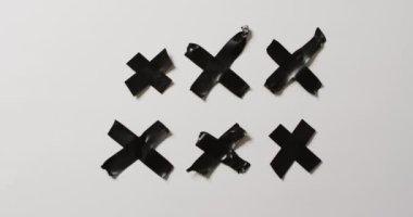 Siyah bandın beyaz arkaplanda haç oluşturduğu video. Kağıt, yazı, doku ve malzeme kavramı.