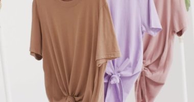 Beyaz arkaplanda asılı beyaz, bej ve mor tişörtlerin yakın çekim videosu. Giyim, moda, perakende, kumaş, doku ve malzeme konsepti.