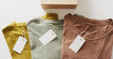 Beyaz arkaplanda etiketli katlanmış tişörtlerin videosu. Giyim, moda, perakende, kumaş, doku ve malzeme konsepti.