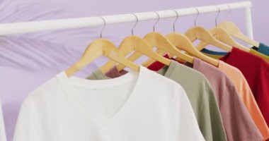 Mor arkaplanda asılı birden fazla tişörtün yakın çekim videosu. Giyim, moda, perakende, kumaş, doku ve malzeme konsepti.