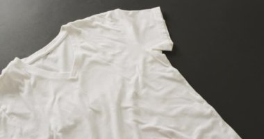 Siyah arka planda beyaz tişörtün yakın çekim videosu. Giyim, moda, perakende, kumaş, doku ve malzeme konsepti.