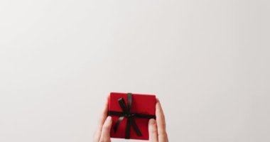 Beyaz arka planda siyah kurdeleyle bağlanmış kırmızı hediye kutusunu yerleştiren ellerin videosu. Sevgililer günü, doğum günü, aşk ve kutlama konsepti.