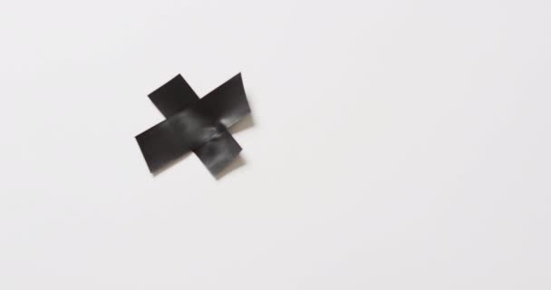 白い背景に十字を形成する黒いテープのクローズアップのビデオ 素材のコンセプト — ストック動画