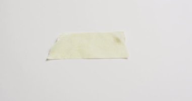 Beyaz arka planda yırtık sarı kağıt parçasının yakın çekim videosu. Kağıt, yazı, doku ve malzeme kavramı.