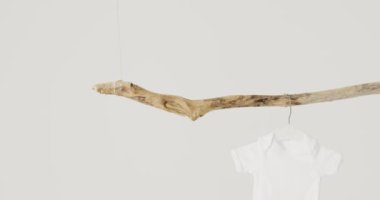 Beyaz bebeğin beyaz arka plandaki dallardan sarkan yakın çekim videosu. Bebek, giysi, moda, kumaş, doku ve malzeme konsepti.