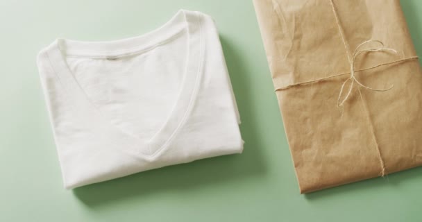 白色折叠T恤与绿色背景的褐色纸包的特写视频 质地和材料概念 — 图库视频影像