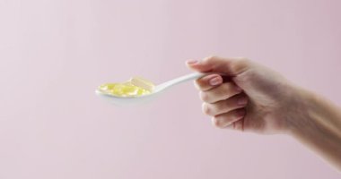 Beyaz yağ kapsüllerinin fotokopi alanlı pembe arka planda tutulduğu video. Tıp, sağlık hizmetleri, sağlık hizmetleri ve sağlık farkındalığı kavramı.