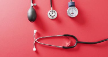 Kırmızı arkaplanda fotokopi uzayı ile sphygmomanometre ile stetoskop videosu. Sağlık hizmetleri, sağlık hizmetleri ve sağlık farkındalığı kavramı.