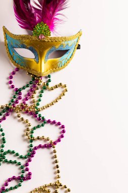 Renkli Mardi Gras boncukları ve beyaz arka planda fotokopi alanı olan karnaval maskesi kompozisyonu. Parti, kutlama ve karnaval konsepti.