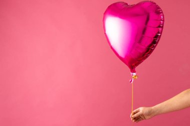El ele tutuşan pembe kalp şeklinde balon pembe arka planda fotokopi alanı ile birlikte yüzüyor. Sevgililer günü, aşk, aşk ve kutlama konsepti.