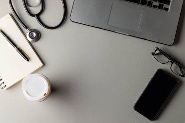 Stetoskop, dizüstü bilgisayar, dizüstü bilgisayar, gözlükler, akıllı telefon ve gri arka planda fotokopi alanı olan kahve. Tıp, sağlık, bilim ve kopyalama alanı konsepti, dijital kompozit resim.