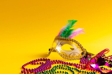 Renkli Mardi Gras boncukları ve sarı arka planda kopya alanı olan karnaval maskeleri. Parti, kutlama ve karnaval konsepti.