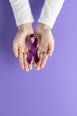 Mor Kanser Farkındalığı kurdelesini tutan ellerin dikey hali. Mor arka planda fotokopi alanı ile. Sağlık hizmetleri, sağlık hizmetleri ve sağlık farkındalığı kavramı.