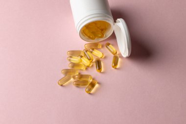 Beyaz hap kutusunun kompozisyonu, pembe arka planda yağ kapsülleri ve fotokopi alanı. Tıp, sağlık hizmetleri, sağlık hizmetleri ve sağlık farkındalığı kavramı.