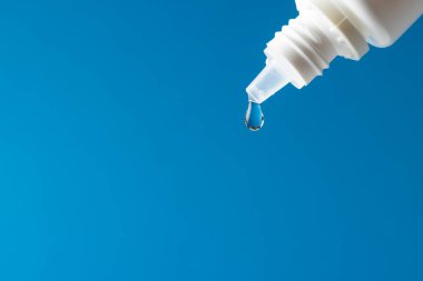 Düşen damlanın bileşimi beyaz şişeden mavi arka plana düşerken fotokopi alanı ile birlikte. Sağlık hizmetleri, tıp, sağlık ve sağlık farkındalığı kavramı.