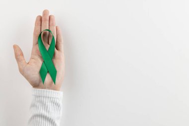 Beyaz arka planda yeşil zihinsel sağlık farkındalığı kurdelesini tutan el kompozisyonu ve kopyalama alanı. Sağlık hizmetleri, sağlık hizmetleri ve zihinsel sağlık farkındalığı kavramı.