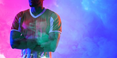 Afrika kökenli Amerikalı erkek futbolcu kollarını kavuşturup dumanlı arka planda duruyor. Boşluğu kopyala, kompozit, spor, futbol, rekabet, neon, duman ve soyut kavram.