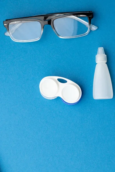 Vertical of glasses with contact lenses case and eye drops and on blue background with copy space. Medical services, healthcare and health awareness concept.