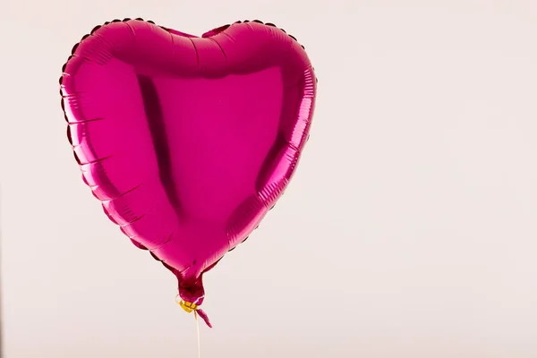 Shiny pink heart shaped balloon floating on white background with copy space. Valentine\'s day, love, romance and celebration concept.