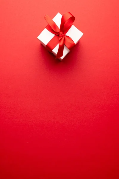 コピースペースのある赤い背景に 赤いリボンで結ばれた白いギフトボックスの垂直方向のオーバーヘッド バレンタインデー ロマンス お祝いのコンセプト — ストック写真