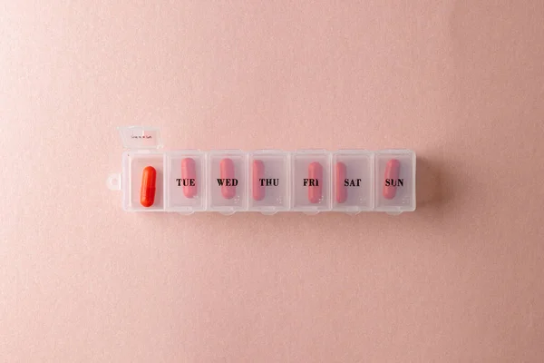 Composition of red pills in weekly pill box on pink background with copy space. Medicine, medical services, healthcare and health awareness concept.