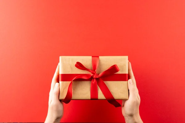 Overhead Hands Holding Gift Brown Paper Red Ribbon Red Background —  Fotos de Stock
