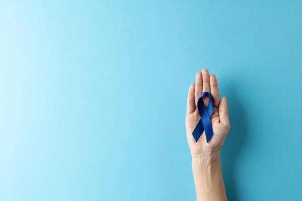 stock image Composition of hand holding blue ribbon on blue background. Medicine, healthcare, science and copy space concept, digital composite image.