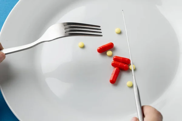 Composition of hands holding fork and knife over plate with various pills. Medicine, medical services, healthcare and health awareness concept.