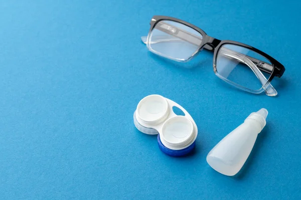 Composition of glasses with contact lenses case and eye drops and on blue background with copy space. Medical services, healthcare and health awareness concept.