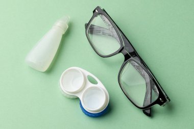 Kontak lens kutulu gözlük bileşimi ve yeşil arka planda solüsyon. Sağlık hizmetleri, sağlık hizmetleri ve sağlık farkındalığı kavramı.