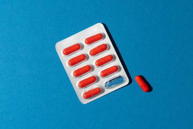 Kabarcık paketindeki kırmızı hapların bileşimi ve mavi arka planda fotokopi alanı olan bir hap. Sağlık hizmetleri, tıp, sağlık ve sağlık farkındalığı kavramı.