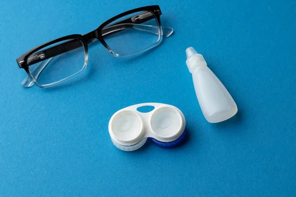 Composition of glasses with contact lenses case and eye drops and on blue background with copy space. Medical services, healthcare and health awareness concept.