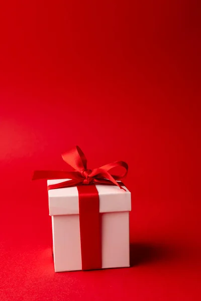 コピースペースと赤の背景に赤いリボンで結ばれた白いギフトボックスの垂直 バレンタインデー ロマンス お祝いのコンセプト — ストック写真
