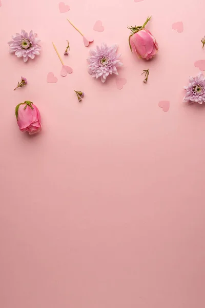 Vertical of pink flowerheads and heart confetti, on pink background with copy space. Valentine\'s day, love, romance, spring and celebration concept.