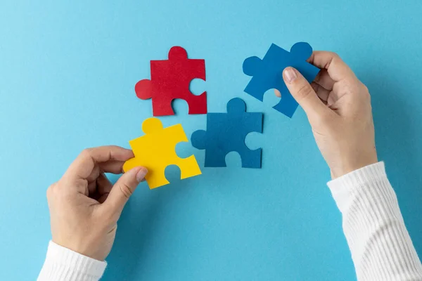 Composition of hands putting jigsaw puzzle pieces together on blue background with copy space. Medical services, healthcare and mental health awareness concept.