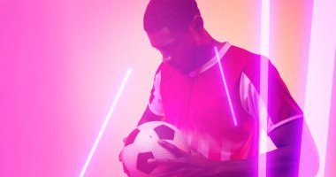 Neon arka planda futbol topu tutan ciddi Afrika kökenli Amerikalı erkek oyuncu üzerine aydınlatılmış çizgiler. Boşluğu kopyala, kompozit, spor, rekabet, çalma, eşleşme, neon ve soyut kavram.
