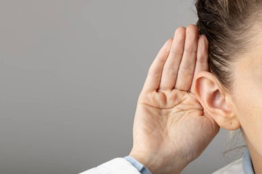 Gri arka planda kulağını tutan Kafkasyalı kadın doktorlara yakın çekim. Tıp, sağlık ve bilim konsepti.